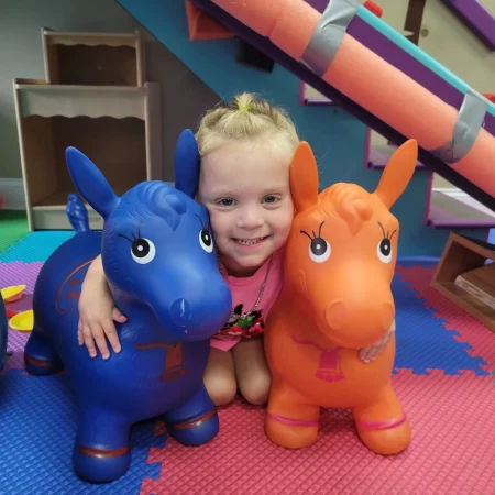 Smiling child posing between blue and orange inflatable hopping animals