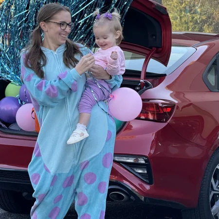 Adult in a blue character costume holding a child at a Halloween event