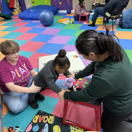 Two therapists supporting a child standing in the therapy gym