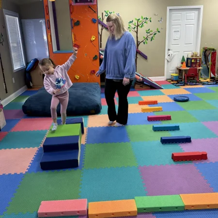 Therapist guiding a child through a colorful balance course
