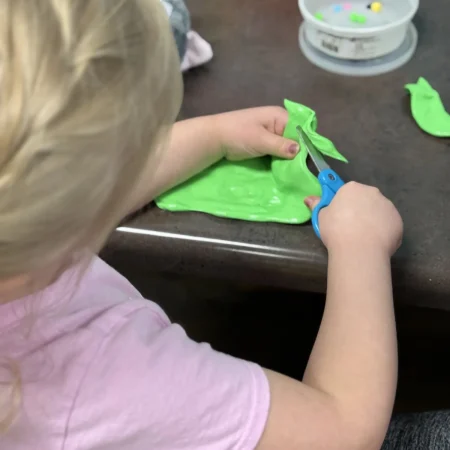 Child practicing scissor skills with green therapy material