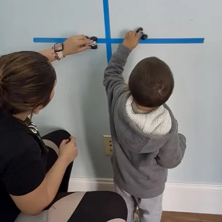 Therapist and child moving toy vehicles along taped direction lines