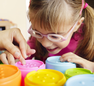 Child in glasses pressing buttons on colourful stacking toys