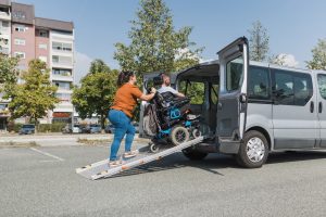 Wheelchair user entering a vehicle by ramp with caregiver support