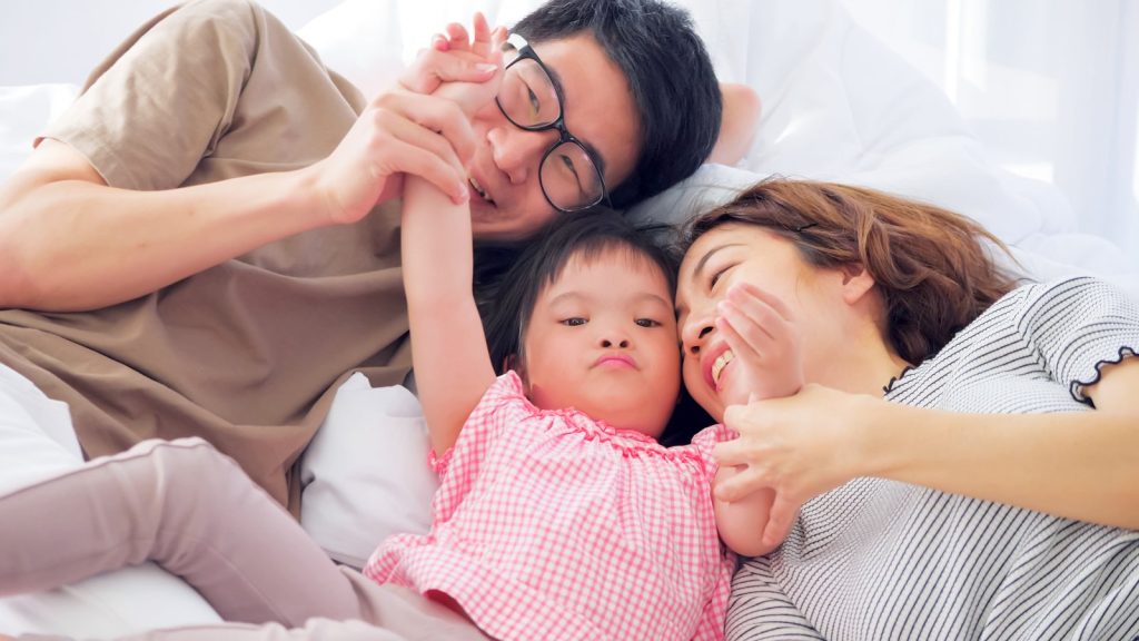 Two parents and their young daughter lying together, laughing